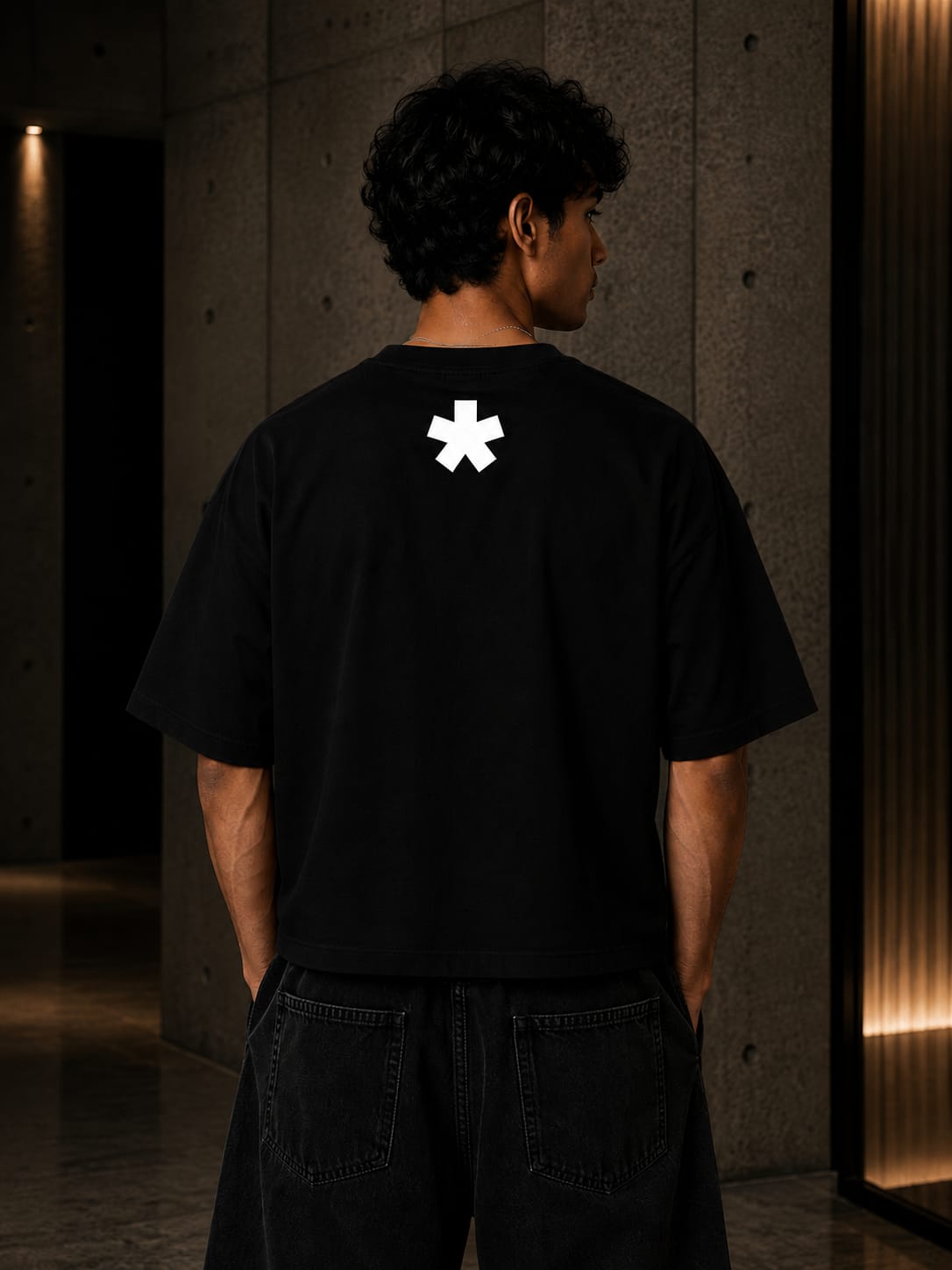 Person wearing a black t-shirt with a white logo on the back in a dimly lit room.
