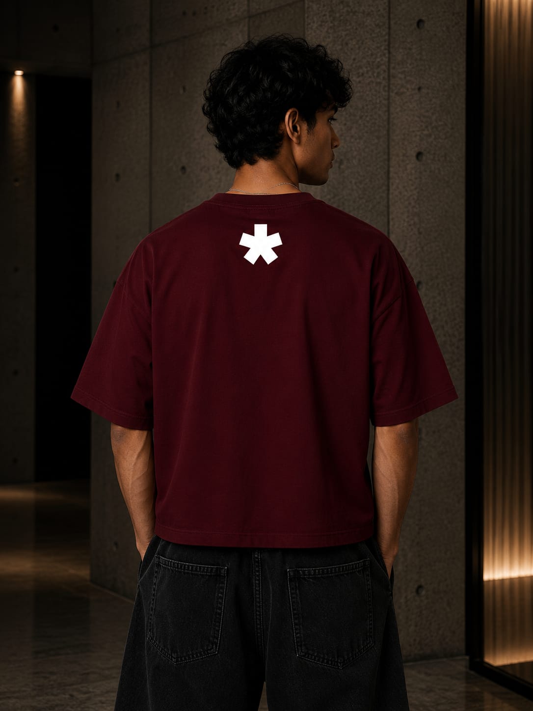 Person wearing a maroon t-shirt with a white logo on the back, standing in a dimly lit room.