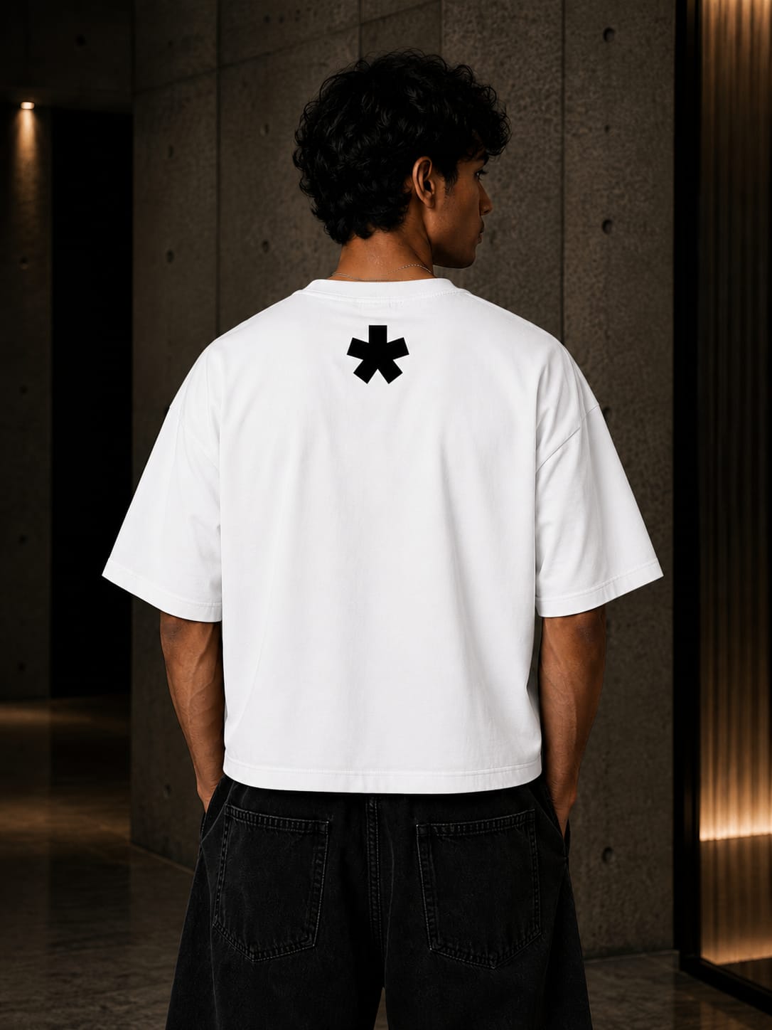 Person wearing a white t-shirt with a black symbol on the back in a dimly lit room.